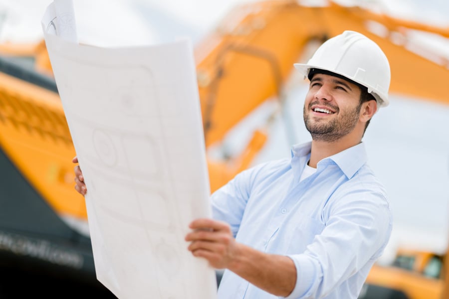 A builder in a hard hat reviewing blueprints on a job site