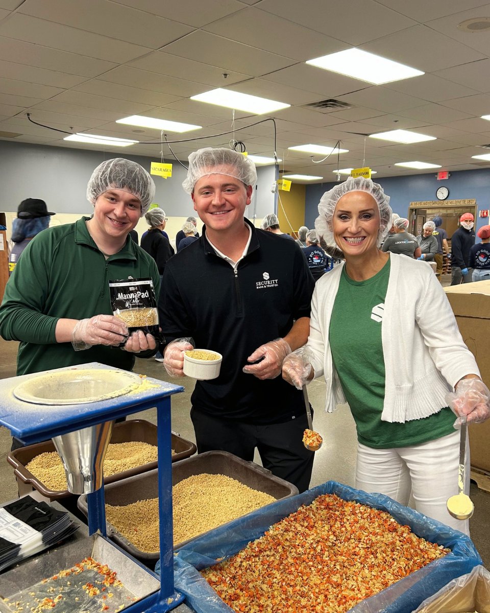 Three Security Bank & Trust Co. volunteers in hairnets filling meal bags at a Feed My Starving Children packing station