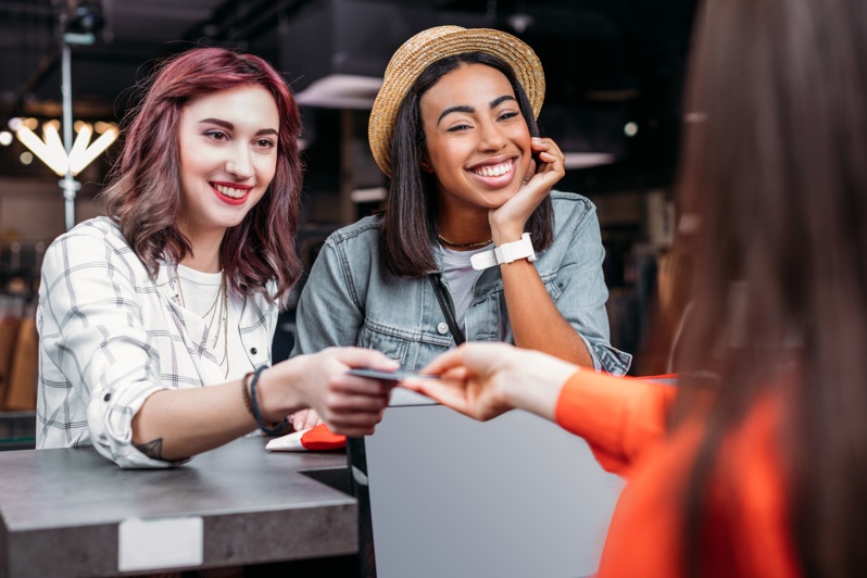 two female friends exchanging a credit card to worker