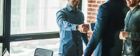 A business owner and a commercial lender shaking hands in a brick office building
