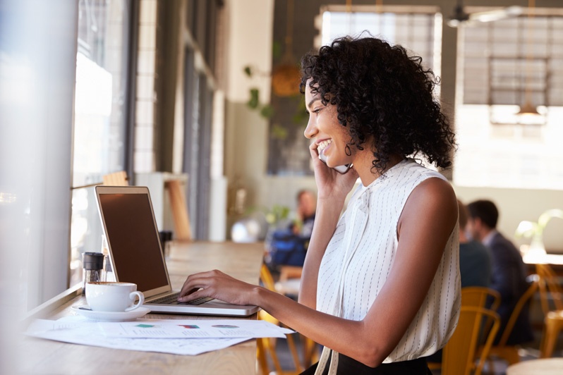 smiling woman on computer at coffee shop next to window