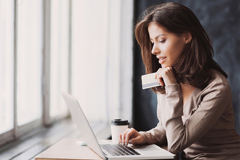 Woman next to window looking at computer with credit card