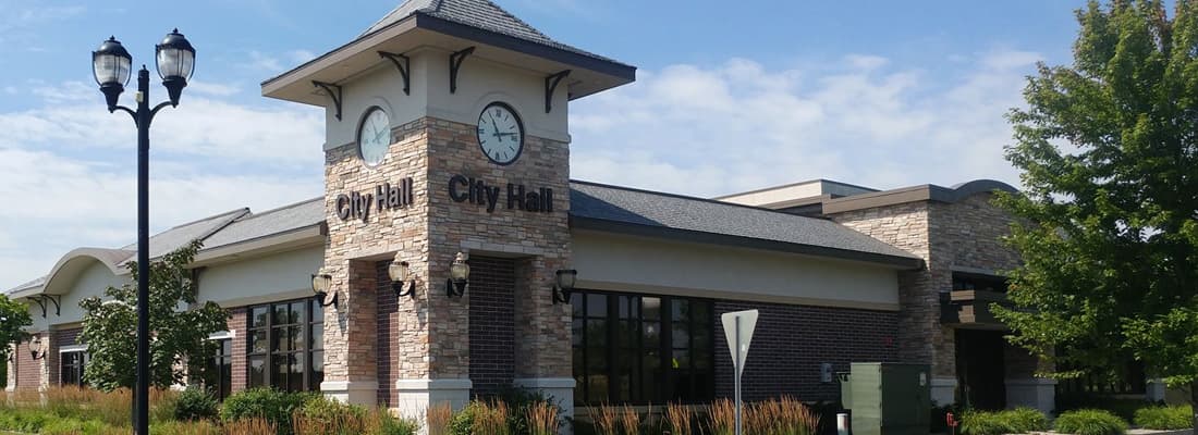 A city hall with a stone clock tower and brick front on a summer morning