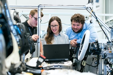 Three engineers review a laptop beside automated production equipment in a manufacturing plant