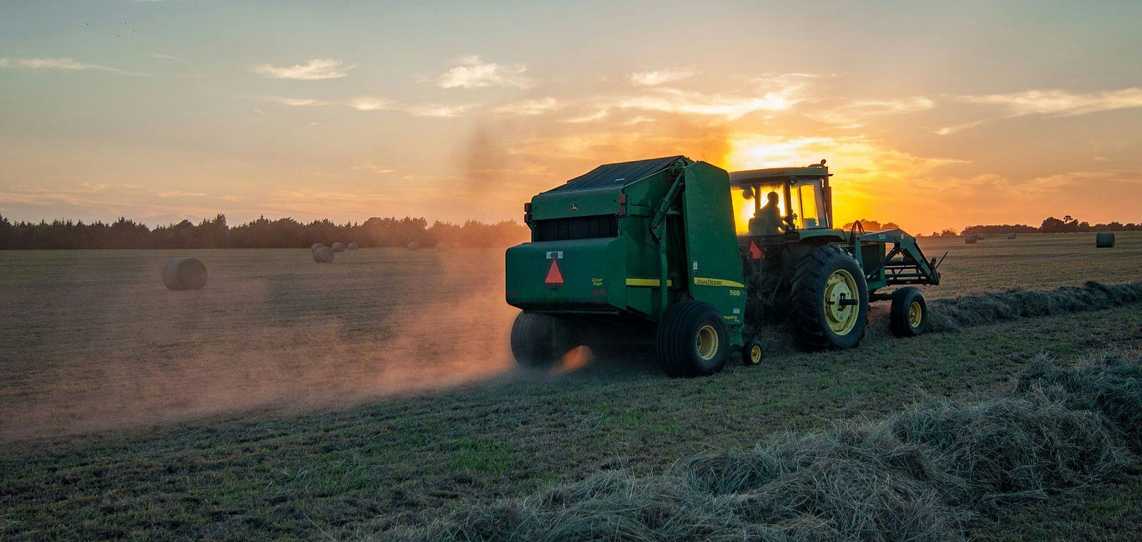 Tractor and baler working a Minnesota hayfield at sunset